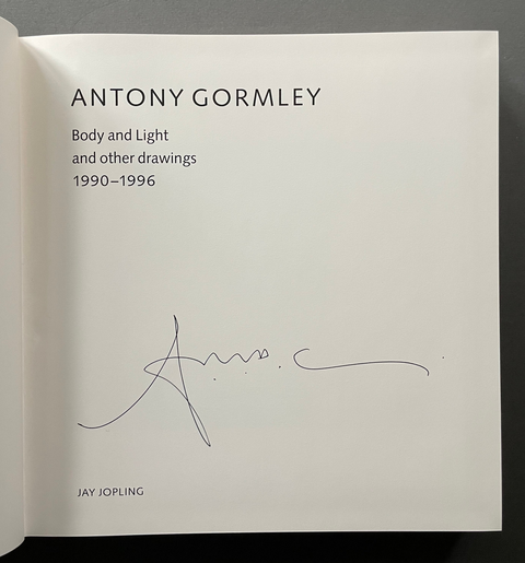An open book or art publication showing a printed page with the text 'ANTONY GORMLEY Body and Light and other drawings 1990–1996' and a visible Antony Gormley signature in blue ink, photographed against a dark gray background.