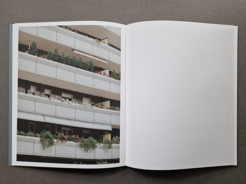 An open book, showing a printed architectural photograph of apartment balconies with plants on the left page and a blank white page on the right.