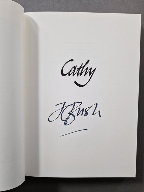 An open book k showing a white page with black cursive signatures reading 'Cathy' and 'JC Bush' on a dark gray background.