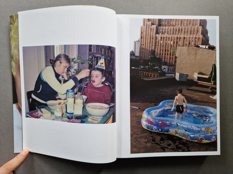 An open book showing two printed photographs side by side. The left page contains a vintage-style photo of a woman feeding a child at a table, and the right page shows a color photo of a child standing in a blue inflatable pool on a rooftop with tall buildings in the background.