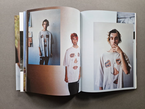 An open book, featuring printed fashion photographs of a person wearing a distressed white T-shirt with torn patch details.