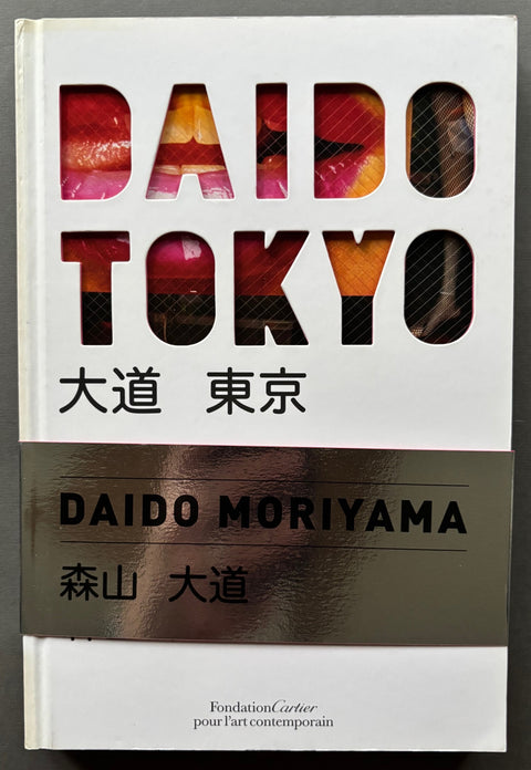 Book titled 'Daido Tokyo' by Daido Moriyama with a white cover, with the title cut of the front board and a silver belly band.