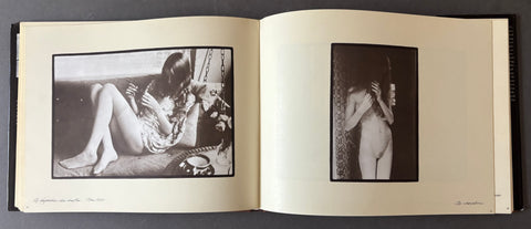 An open vintage art book or photo album laid flat on a dark surface, showing two black-and-white photographic prints mounted on cream pages.