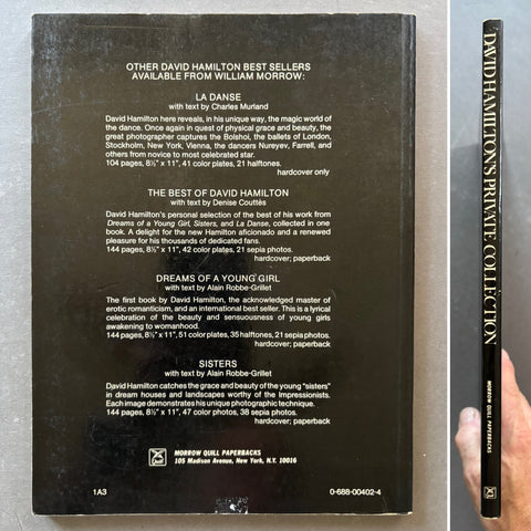 Back cover of a hardcover book showing a black background with white text listing David Hamilton best sellers and the spine of a matching book standing vertically on the right, with a hand holding the spine.