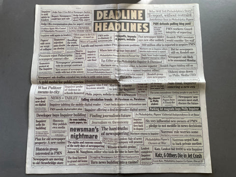 A folded newspaper with multiple columns of dense black text on a white background, photographed from above on a neutral surface.