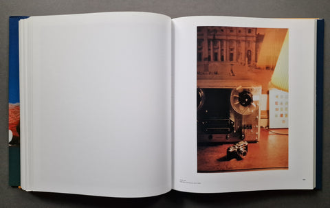 An open book, showing a mostly blank white left page and a printed photograph on the right page featuring a vintage camera in a warm-toned interior scene.