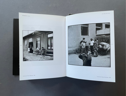 An open book or photo album laid flat on a dark gray surface, showing two printed black-and-white photographs on white pages.