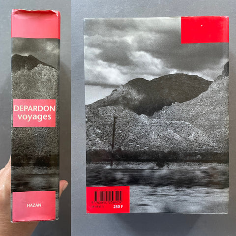 A book titled 'DEPARDON voyages' by Hazan is shown standing upright next to its front cover, held by a hand on the left. The cover features a black and white landscape photograph of mountains and water, with a bright red band at the top and a matching red barcode label at the bottom.