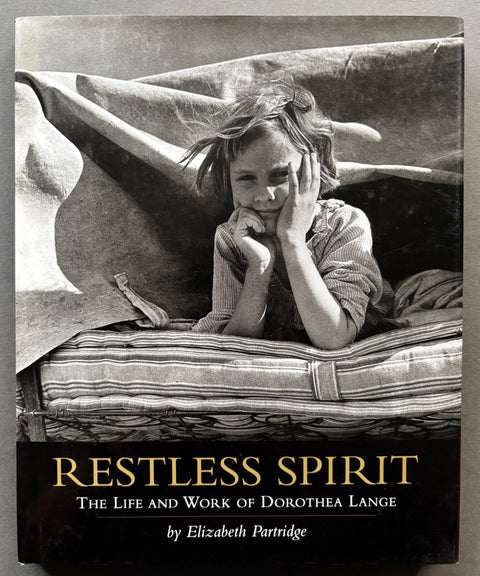 Book titled 'Restless Spirit: The Life and Work of Dorothea Lange' with a cover featuring the black and white image of a girl resting on a mattress.