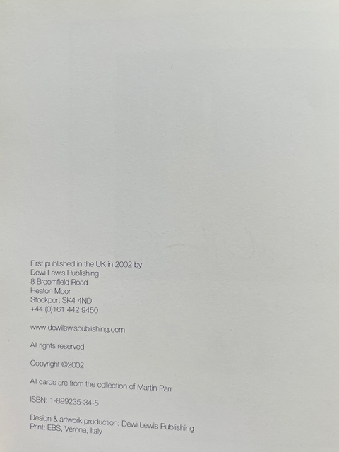 A hand holding a red book or booklet open to a white interior page with small printed copyright and publication details, photographed against a dark gray background.
