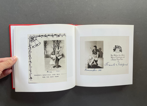 An open vintage book or album with white pages, showing two black-and-white printed photo panels and handwritten text. A hand is holding the left edge of the book against a dark gray background.