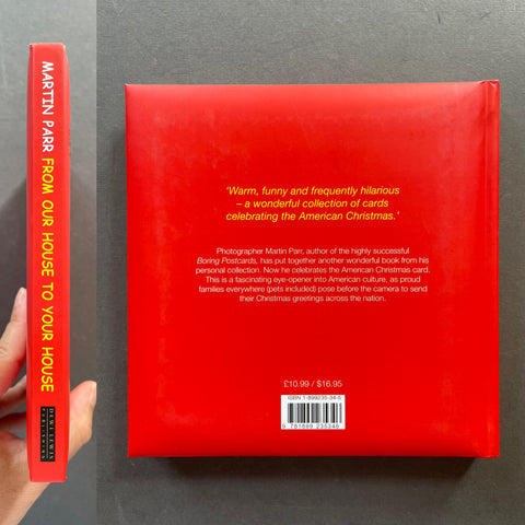 A hardcover book titled 'From Our House to Your House' by Martin Parr, shown with its red back cover and spine held by a hand against a dark gray background.