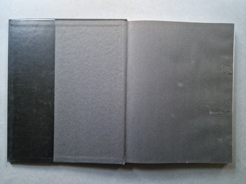 A square dark gray textured panel or mat shown open flat against a light gray background, with a black rectangular piece partially visible on the left.