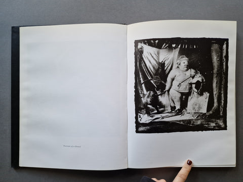 An open book showing a black-and-white photographic print on the right page with a visible human finger pointing at it.