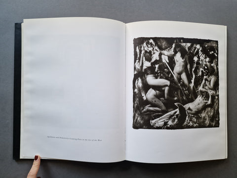 An open book showing a black-and-white reproduction of a classical sculpture on the right page, with a hand holding the left page against a dark gray background.