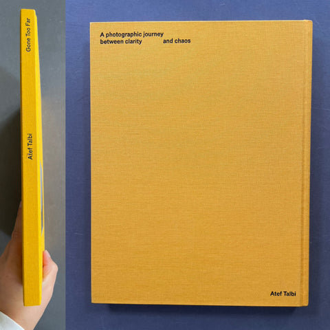 A hardcover book titled 'A photographic journey between clarity and chaos' by Atef Talbi, shown standing upright with its front cover and spine visible against a dark blue background. A hand is holding the left edge of the spine to show thickness.