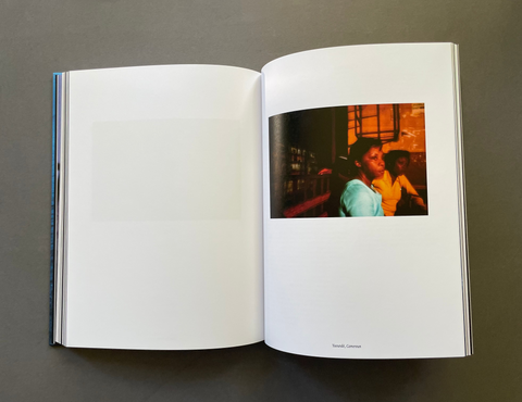 An open hardcover book laid flat on a dark gray surface, showing a mostly blank white left page and a printed photo page with a warm-toned portrait on the right. The book spine is visible on the left edge.