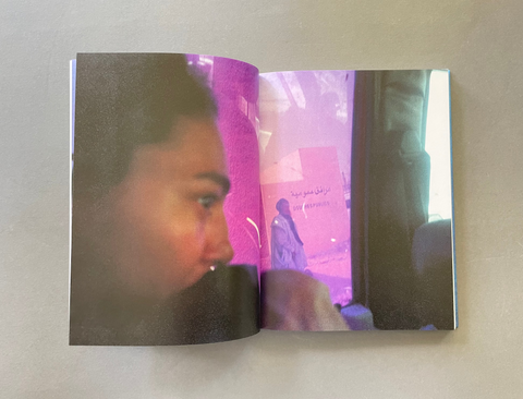 An open printed book or photo album laid flat on a light neutral surface, showing two glossy printed pages with a stylized close-up portrait in pink and purple tones.