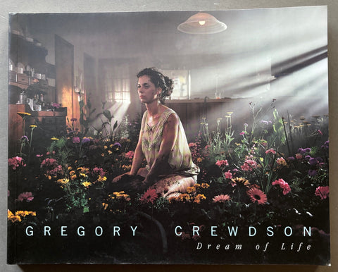 Book titled 'Dream of Life' by Gregory Crewdson with a cover featuring the image of a woman sitting in a bed of flowers inside a kitchen.
