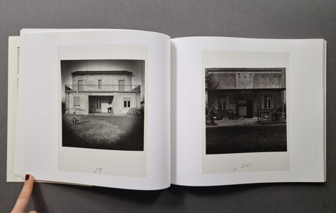 An open book showing two black-and-white architectural photographs printed on white pages, photographed against a dark gray background. 