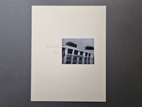 An original black and white silver gelatin print on an off-white mount, featuring a small black-and-white photograph of a building reflected in water, with handwritten text to the left saying "asslicking slut".