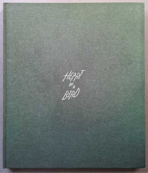 A square hardcover book with a textured green surface and the title 'Heart of a Bird' printed in white script near the center.