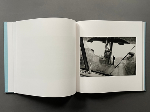 An open hardcover book laid flat on a dark gray surface, showing a large blank white page on the left and a black-and-white photographic print on the right.