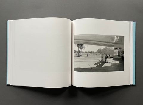 An open book or photo journal laid flat on a dark gray surface, showing blank white pages on the left and a black-and-white photographic print on the right.