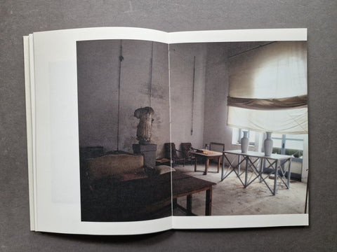An open book spread showing a large interior photograph of a dimly lit room with tables, chairs, and a draped window treatment, photographed against a dark gray background.