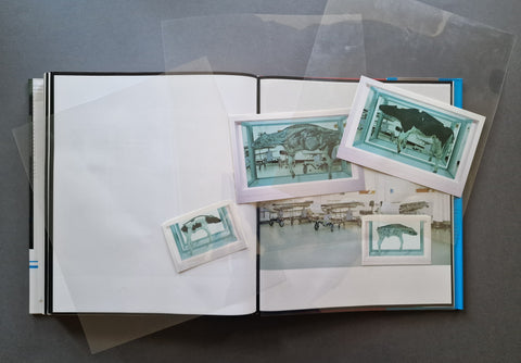 An open photobook laid flat with several translucent plastic sheets partially covering the pages and three printed photo inserts showing vintage aircraft scenes in blue-green tones.