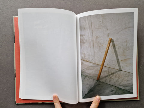 An open book showing a blank white page on the left and a photograph of a wooden easel leg against a textured wall on the right