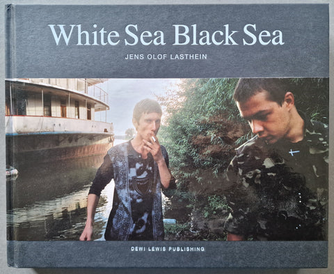 The black hardback cover of White ea Black Sea by Jens Olof Lasthein featuring a portrait of two you man (one smoking a cigarette) next to a boat.