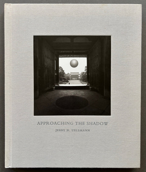 Book titled 'Approaching the Shadow' by Jerry N. Uelsmann with a grey cover featuring the tipped in image of the entrance to a building looking out from the inside.