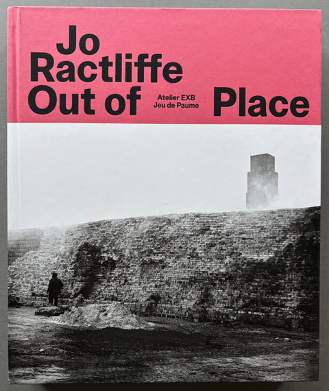 Book titled 'Out of Place' by Jo Ractliffe with a pink and black and white cover featuring the image of a wall and tower stack.