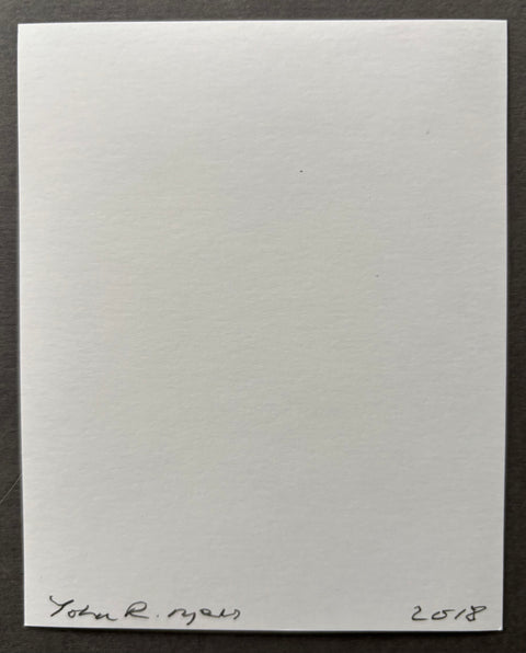 A blank white square card or paper with handwritten signature and the year 2018 at the bottom, photographed against a dark gray background.