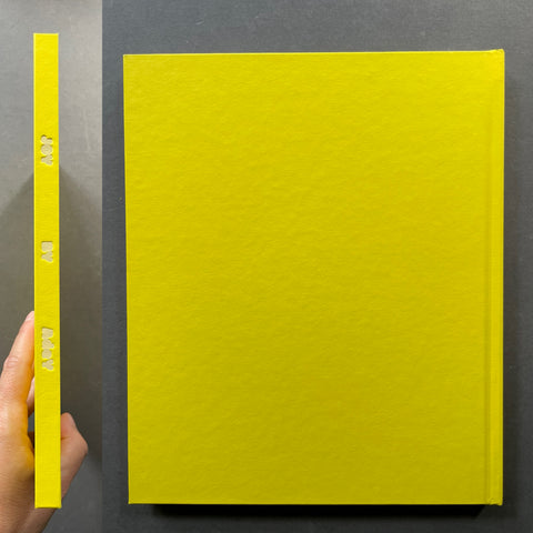 A bright yellow hardcover book or journal shown standing upright, with a hand holding the spine on the left to demonstrate its thickness. The cover is textured and features the title 'THE ART OF AI' embossed vertically on the spine.