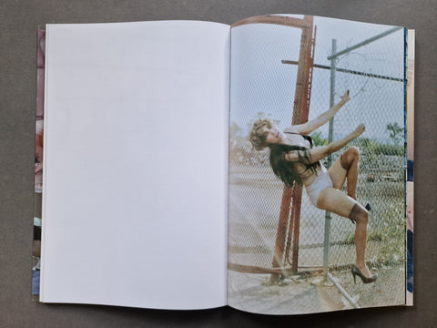 An open book, showing a large white left page and a printed photo on the right page of a woman posing behind a chain-link fence outdoors.