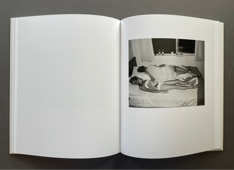 An open hardcover book lying flat on a dark gray surface, showing a black-and-white photograph printed on the right page of a blank white spread.