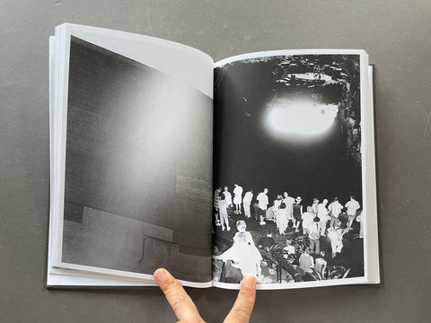 An open black and white art book or photo magazine held open by a hand, showing two photographic pages against a dark gray background.