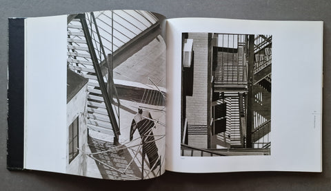 An open book spread laid flat on a dark surface, showing two black-and-white architectural photographs printed on white pages.