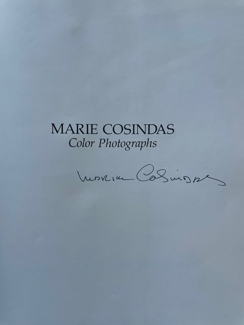 A book cover or printed publication page with the title 'MARIE COSINDAS Color Photographs' in black serif text and a handwritten signature below, on a pale blue background.