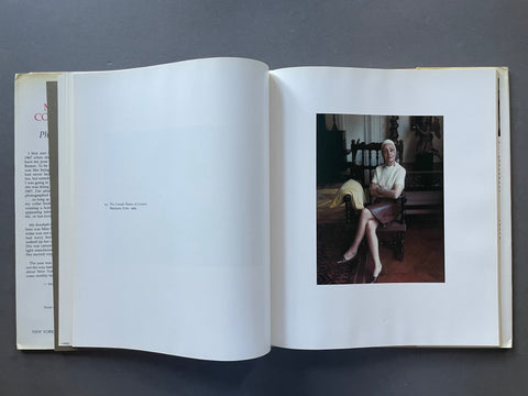 An open book laid flat on a dark gray surface, showing a printed interior spread with mostly blank white pages and a small color photograph on the right page of a woman seated indoors.