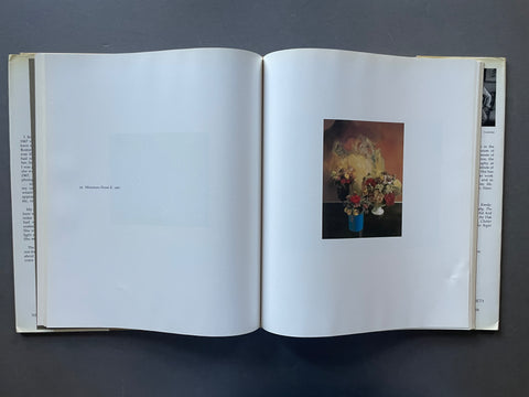 An open art book or magazine laid flat on a dark gray surface, showing a printed still life painting of flowers in blue vases on the right page.