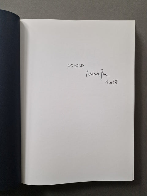 An open book showing a white interior page with the printed word 'OXFORD' and a handwritten signature and date, photographed against a dark gray background.