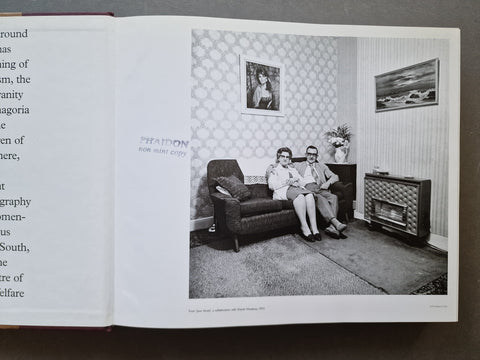 An open book spread from Martin Parr by Val Williams showing a black-and-white interior photograph of a couple sitting on a sofa in a vintage living room, with stamp on top "Phaidon non mint copy"