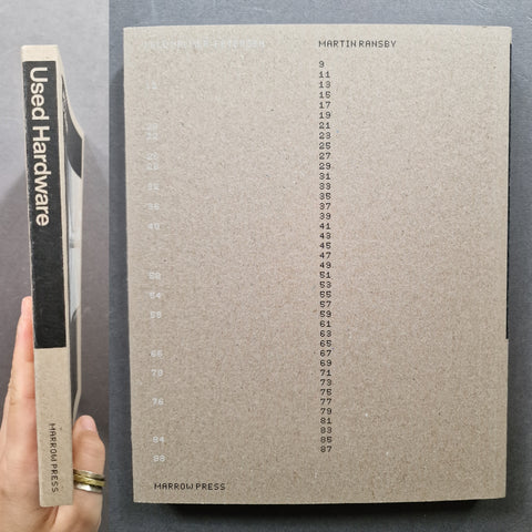 A hand holds a used copy of Martin Rinsey's 'Used Hardware' book by Harrow Press. The book has a textured, warm gray-brown cover with a black spine band on the left side displaying the title and author in white.