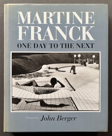 Book titled 'One Day To The Next'by Martine Franck with a grey cover featuring the image of people relaxing around a swimming pool.