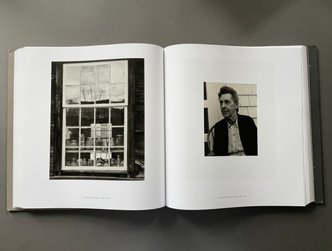 An open hardcover book laid flat on a dark gray surface, showing two black-and-white printed photographs on white pages.