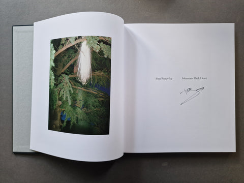 An open art book showing Rozovsky's signature on the right. The left page shows a square photographic print of a white hanging mass of fur or fibers among green tree branches.