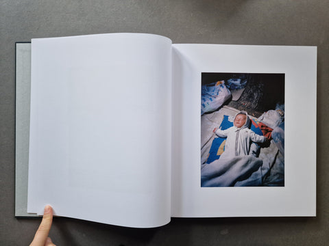 An open book, showing a large blank white page on the left and a printed photograph on the right of a baby lying on blue and white bedding.
